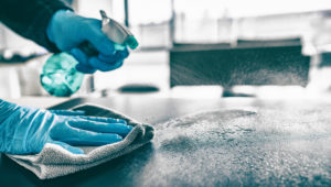 Sanitizing table surface with disinfectant spray bottle washing surfaces with towel and gloves. 